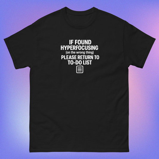 Black T-shirt with white text reading 'If found hyperfocusing on the wrong thing, please return to to-do list' with notepad icon, flat lay product mockup