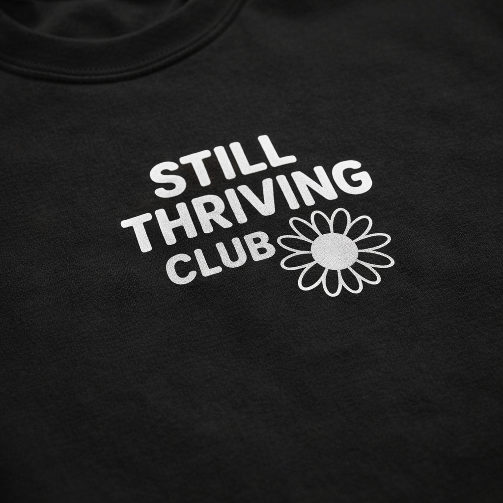 Close-up of the white Still Thriving Club logo and flower printed on black fabric, highlighting the texture of the t-shirt.