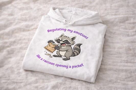 Folded white hoodie laid on fabric background with raccoon illustration and purple text about regulating emotions