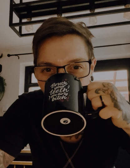 Person holding the “Brush Your Teeth You Dirty Bitch” black mug by Still Thriving Club in an indoor setting.