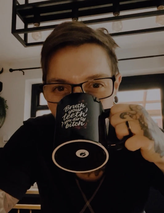 Person holding the “Brush Your Teeth You Dirty Bitch” black mug by Still Thriving Club in an indoor setting.