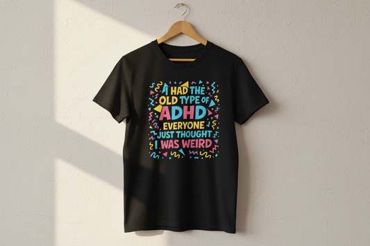 Black ADHD graphic t-shirt hanging on a wooden hanger against a light wall with natural sunlight