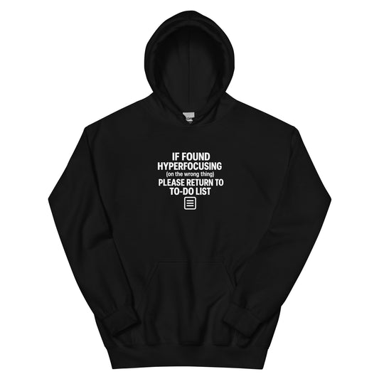 Black hoodie with white text reading 'If found hyperfocusing on the wrong thing, please return to to-do list' with notepad icon, flat lay product mockup