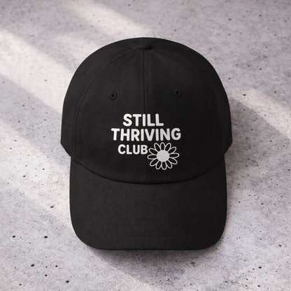 Top-down view of a black Still Thriving Club baseball cap showing the curved brim and white embroidered logo centered on the front panel.