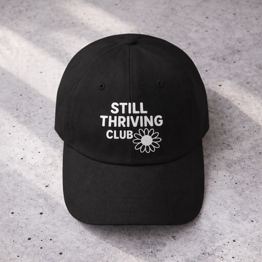 Top-down view of a black Still Thriving Club baseball cap showing the curved brim and white embroidered logo centered on the front panel.