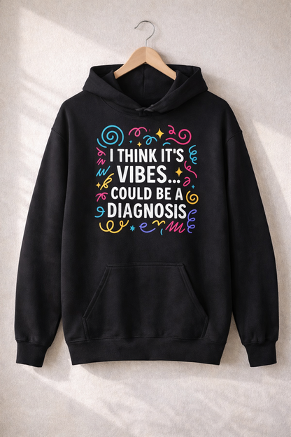 Black unisex hoodie hanging on a wooden hanger featuring the text “I think it’s vibes… could be a diagnosis” in colourful, swirly lettering.