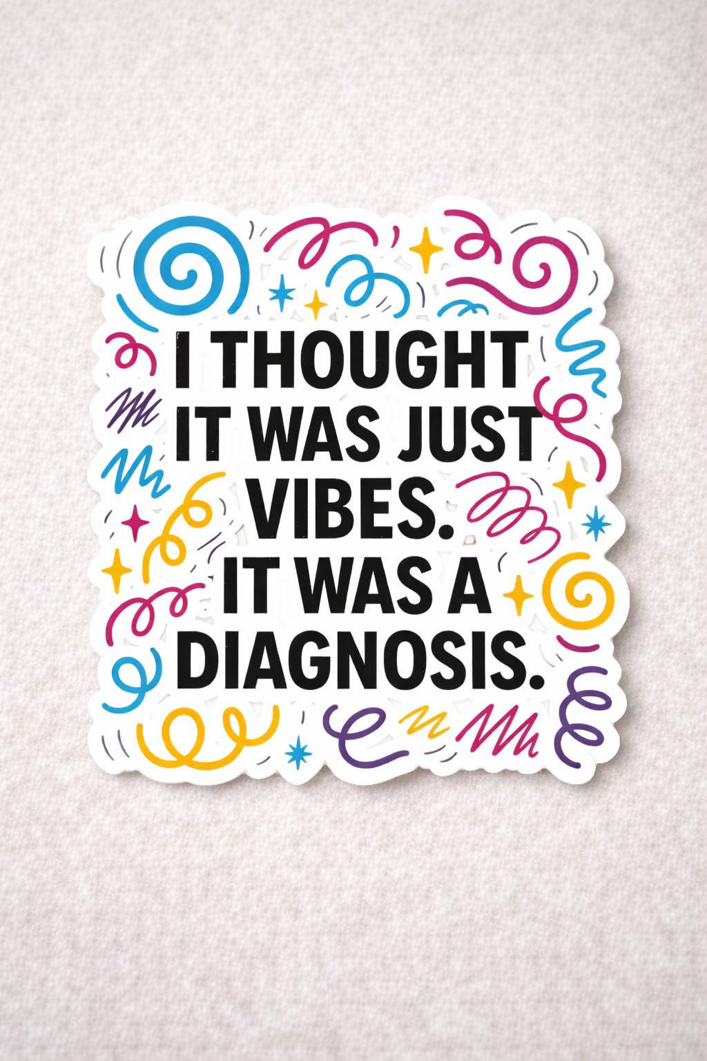 Vinyl sticker reading “I thought it was just vibes. It was a diagnosis” with colourful swirls and stars on a light textured background
