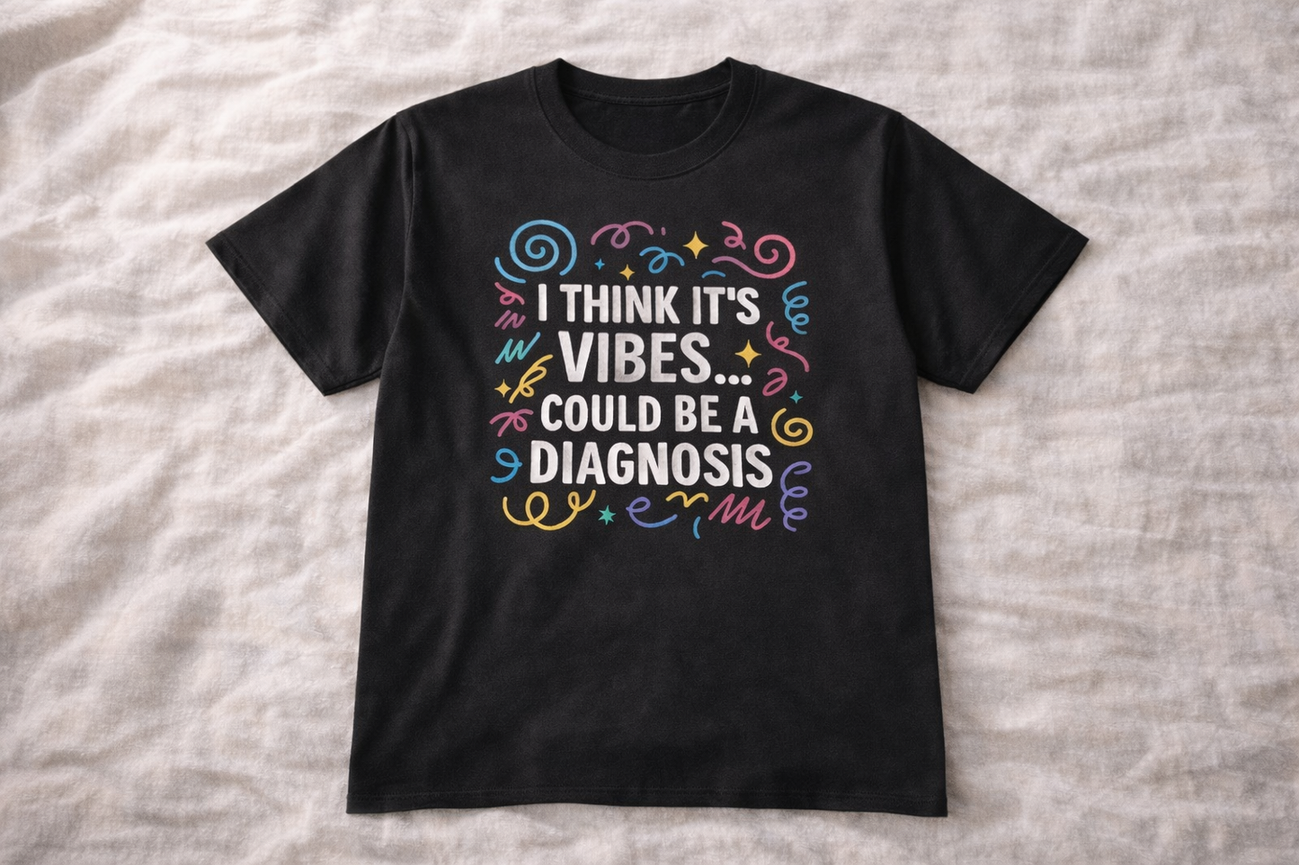 Black t-shirt laid flat on fabric background with colourful text design saying “I think it’s vibes… could be a diagnosis”.