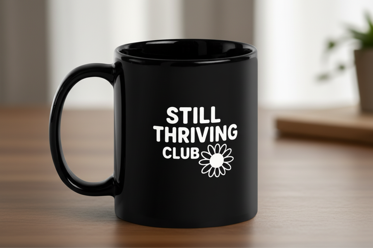 Black glossy ceramic mug featuring the Still Thriving Club logo, shown on a wooden surface with the handle visible from the side.