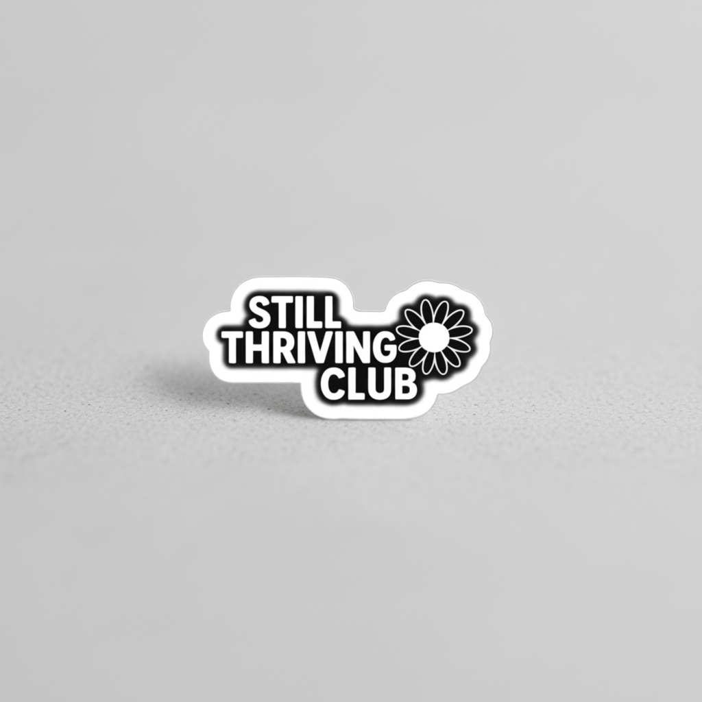 Black and white Still Thriving Club logo sticker photographed on a neutral light grey surface, showing the full sticker shape and design clearly.